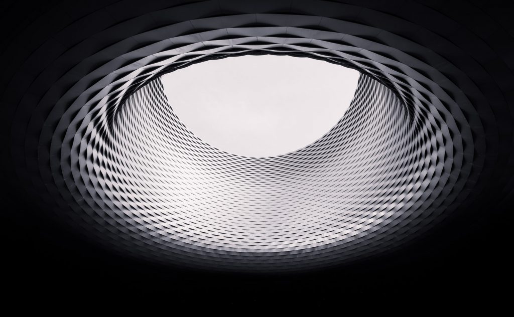 Geschwungene Metallfassade mit ovaler Öffnung zum Himmel in Schwarzweiß