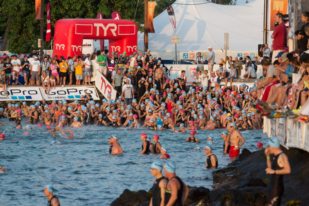 Hunderte Triathleten im Wasser beim Schwimmstart, Zuschauer am Ufer