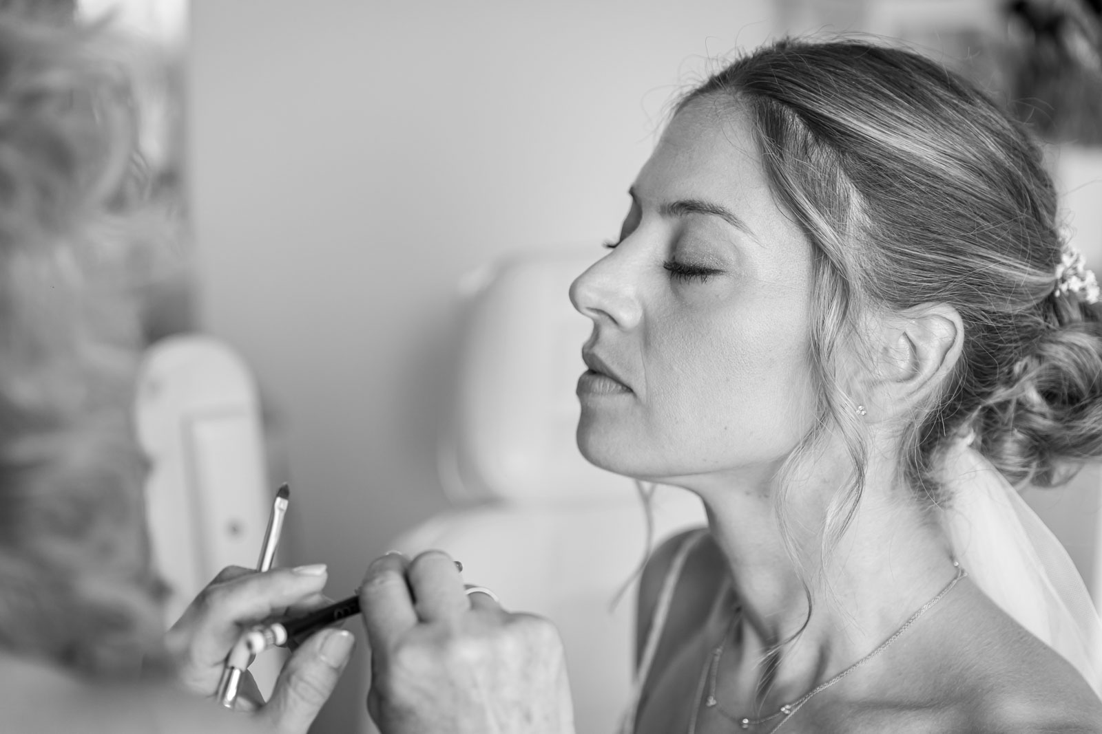 Braut mit geschlossenen Augen beim Make-up am Hochzeitsmorgen