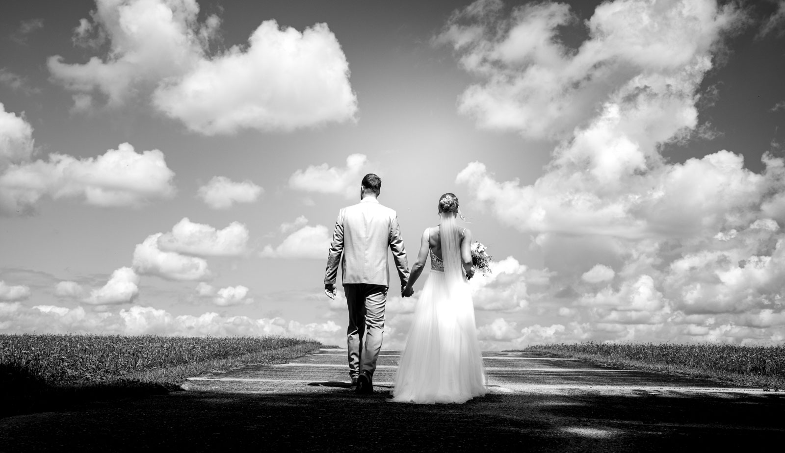 Brautpaar geht Hand in Hand auf einem Feldweg unter Wolken, Schwarzweiß