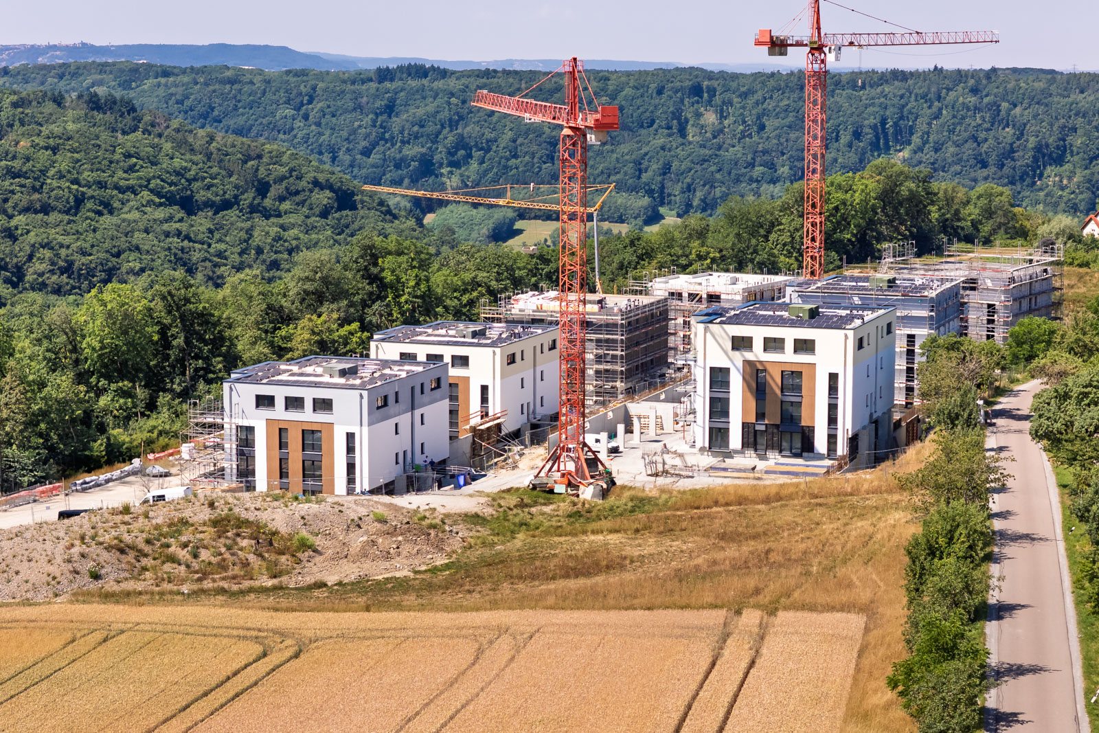 Luftaufnahme einer Wohnanlage im Bau mit zwei Kränen am Waldrand